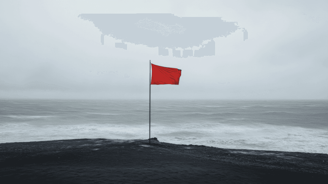 Röd flagga på klippa framför stormigt hav.